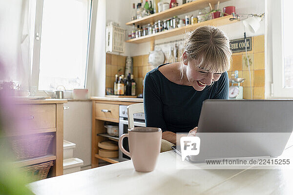 Laughing woman using laptop in the kitchen