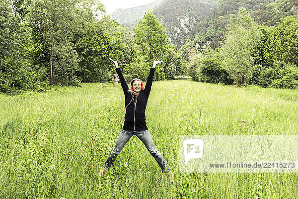 Happy young woman with red headphones jumping in the air on a meadow  Baitoni  Italy