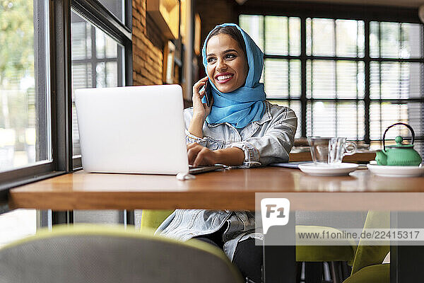 Businesswoman wearing turquoise hijab in a cafe and working with her laptop  on the phone