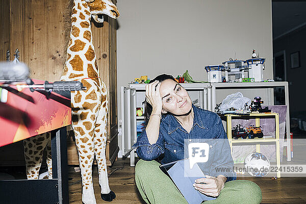 Mother sitting in a children s room at home with a giraffe toy and a tablet