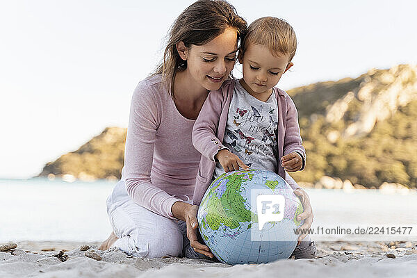 Mother and little daughter looking together at Earth beach ball