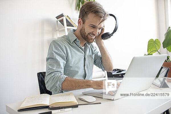 Smiling man with headphones and laptop at desk in office