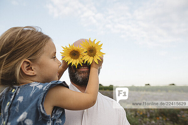 Daughter covering eyes of father with sunflowers