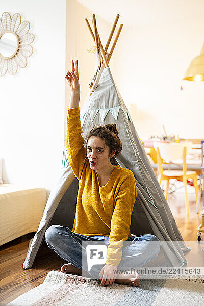 Young woman sitting in a cosy home setting  making a peace sign in front of a tipi tent