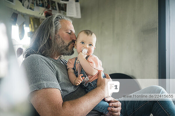 Happy mature man kissing baby girl at home