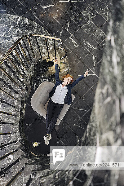 Top view of cheerful businesswoman sitting in armchair at staircase
