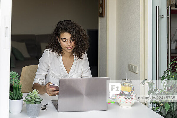 Young woman using cell phone and laptop at desk