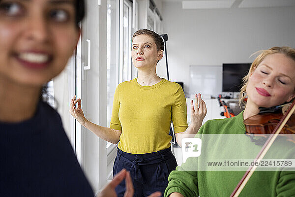 Women practicing yoga and playing violin in an office setting