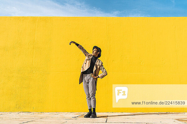 Young man dancing in front of yellow wall  taking selfies