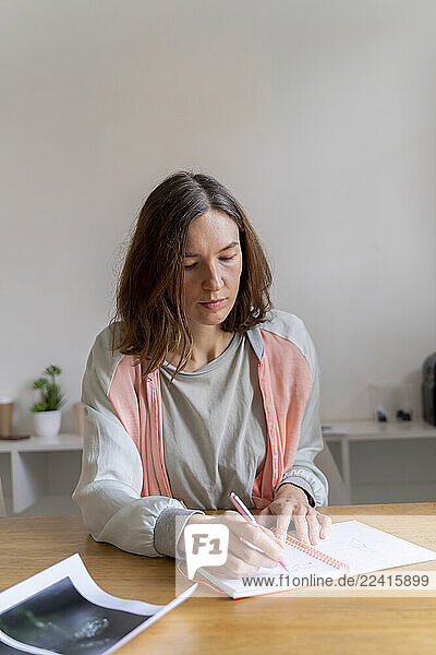 Woman writing in notebook at table in office