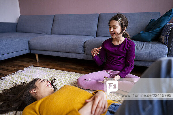Big sister and little sister relaxing at home on the carpet with a smartphone