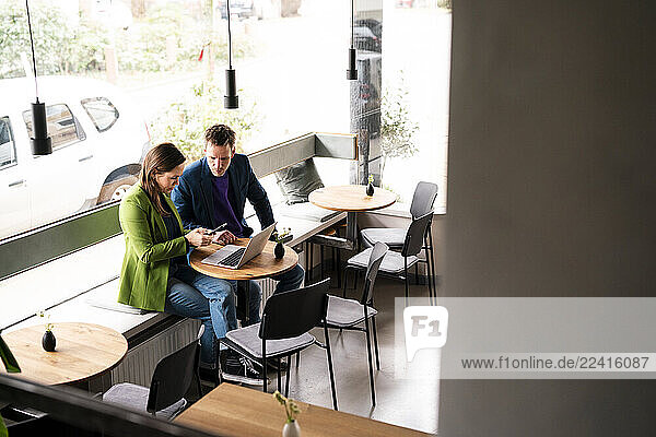 Two people working with a laptop and smartphone in a café