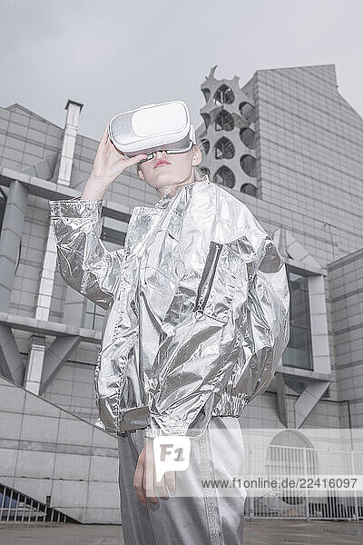 Girl in silver suit. looking through VR goggles in futuristic city
