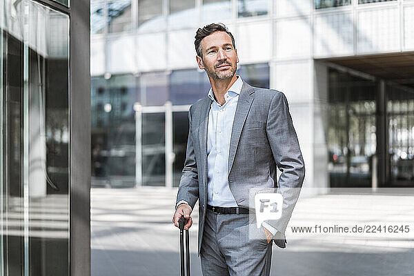 Businessman in a suit standing outdoors with a suitcase