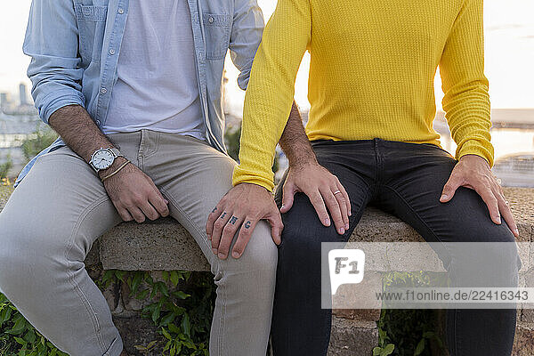 Close-up of affectionate gay couple sitting on a wall