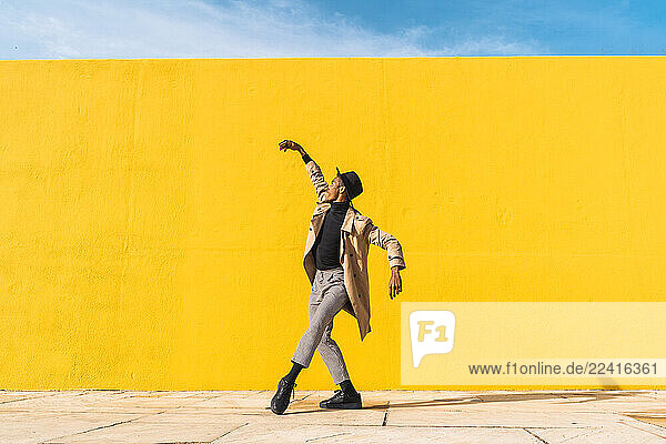 Young man dancing in front of yellow wall  taking selfies