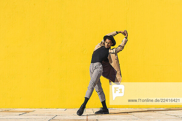 Young man dancing in front of yellow wall