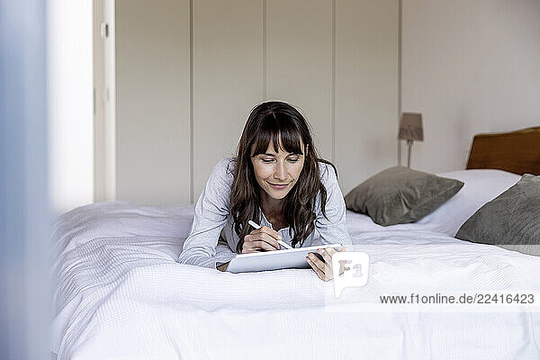 Relaxed woman lying on bed at home using tablet