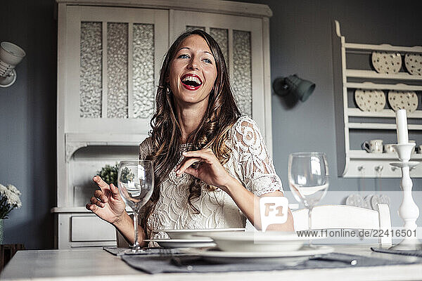 Portrait of laughing young woman sitting at laid table in country style kitchen