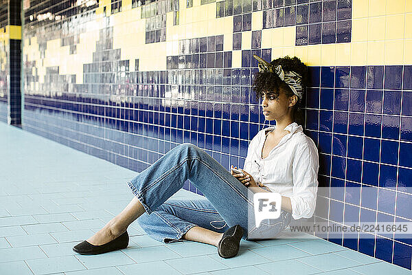 Portrait of young woman sitting on tiled floor listening music with earphones and smartphone
