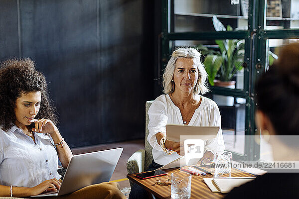 Businesswomen working together in loft office handing over papers