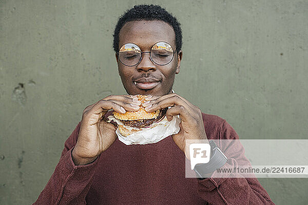 Young man eating cheeseburger  with eyes closed