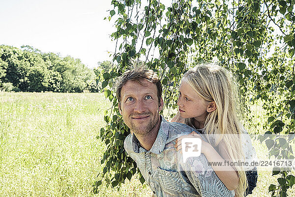 Father carrying daughter piggyback under a birch tree