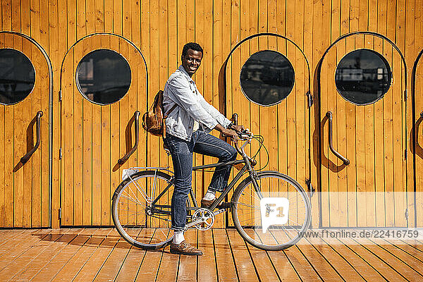 Young man riding bicycle in front of wooden doors