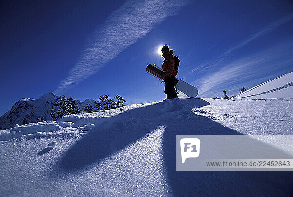 A female snowboarder hiking in the backcountry with her snowboard on her way to go snowboarding.
