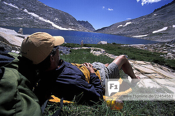 A hiker laying down and relaxing in an alpine meadow by a lake in Eastern Sierra Nevada mountains  California.