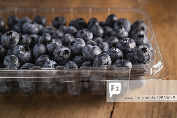 Blueberries in plastic sales container on wooden table