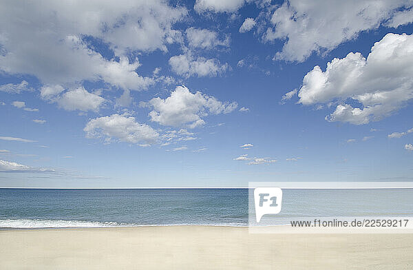 Puffy clouds over empty beach and calm ocean
