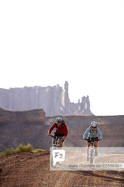 Mountain bikers Brad Barlage and Katie Caviccio ride below sandstone towers on the White Rim Trail in Canyonlands National Park  Utah.