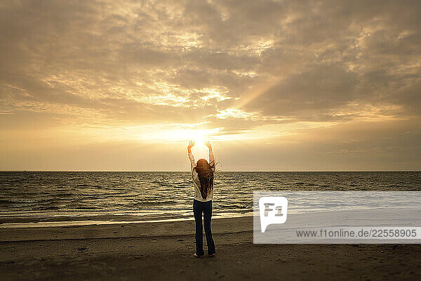 Tween girl long hair reaching towards sunset on beach Outer Bank