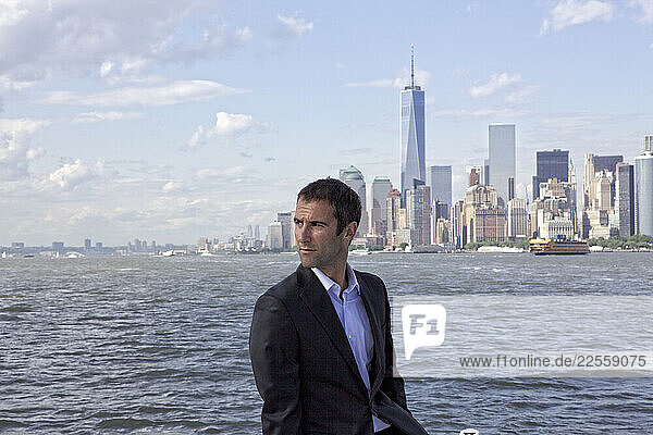 Portrait of man in suit on boat in front of New York city skyline.