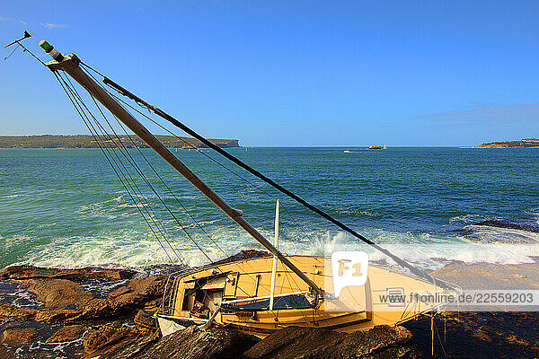 The ketch Bide a Wee aground on her side with holes in her timber hull on the rocks at Grotto Point near Dobroyd Head at Balgowlah Heights Sydney after a storm.