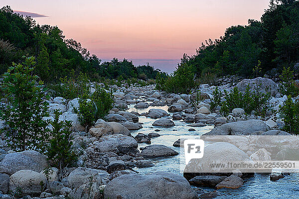 River flowing through rocks at sunset with pink and purple sky