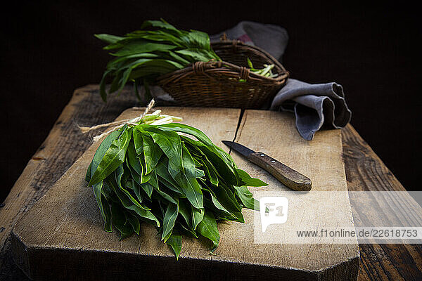 Bundle of wild garlic on a rustic cutting board with a knife and willow basket