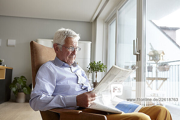 Senior man reading a newspaper indoors in a bright living room