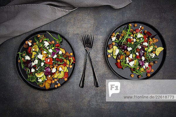 Two plates of Mediterranean salad with roasted vegetables and sheep cheese on a table