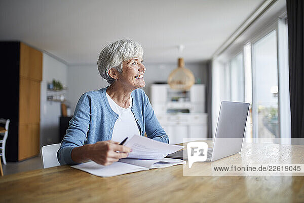 Senior woman at home using laptop and reviewing documents