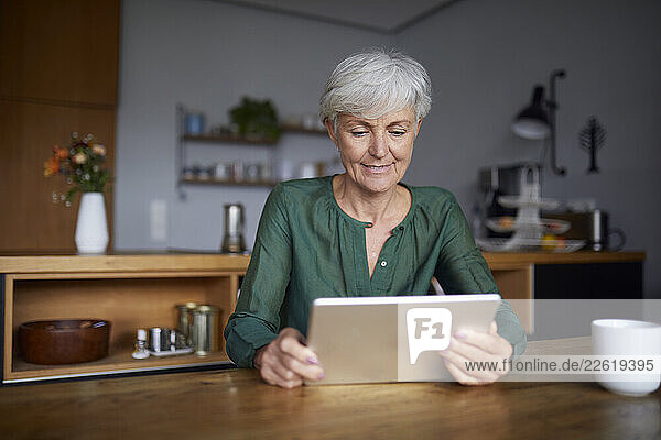 Woman in green shirt using tablet at home in kitchen