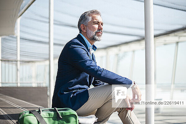 Mature businessman sitting outdoors with a travelling bag  looking thoughtful