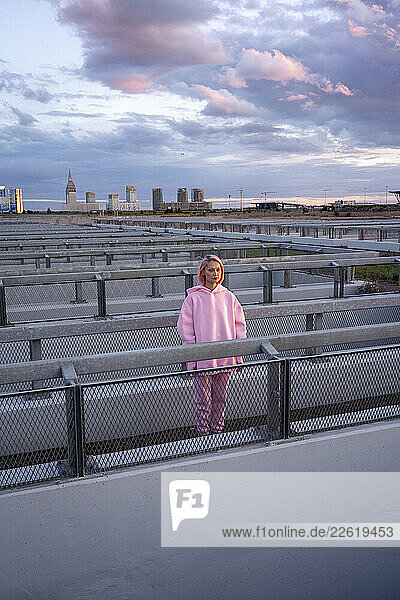 Young woman with pink hair wearing pink hooded shirt standing at railing