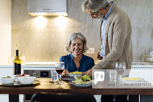 Mature man serving dinner to his wife in kitchen at home
