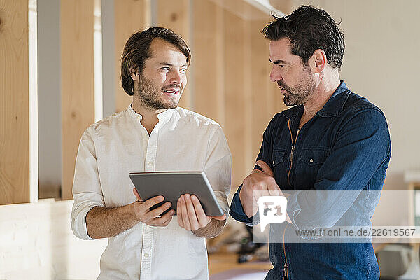 Two businessmen with tablet talking in wooden open-plan office