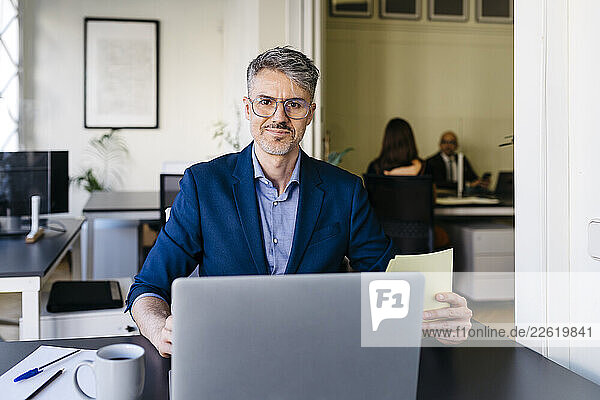 Smiling confident businessman working on laptop at office desk