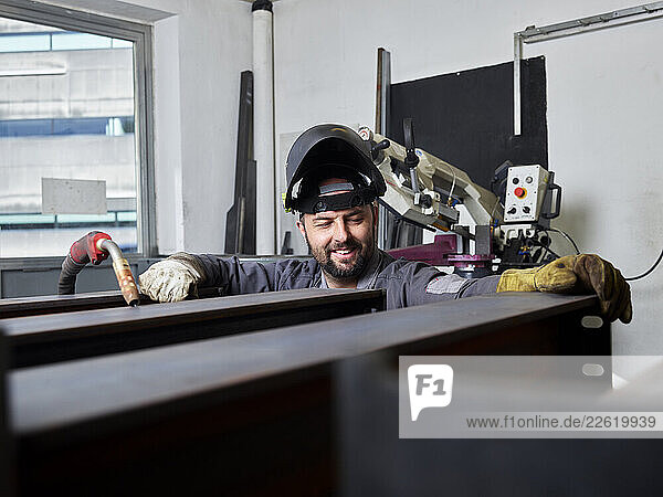 Welding technician laughing while working in his workshop with protective equipment