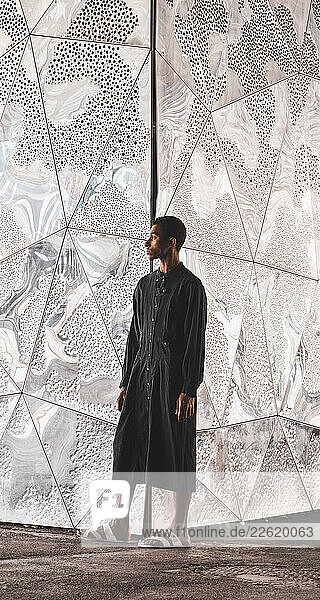 Young man wearing black kaftan standing at structured wall
