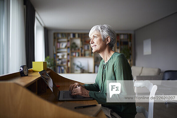 Woman at home using laptop and pondering in a serene setting